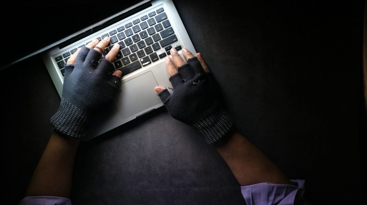 A person wearing fingerless gloves typing on a laptop on a dark surface