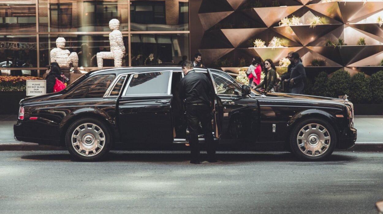 Elegant Rolls Royce with chauffeur outside modern building in New York City, illustrating luxury and class.