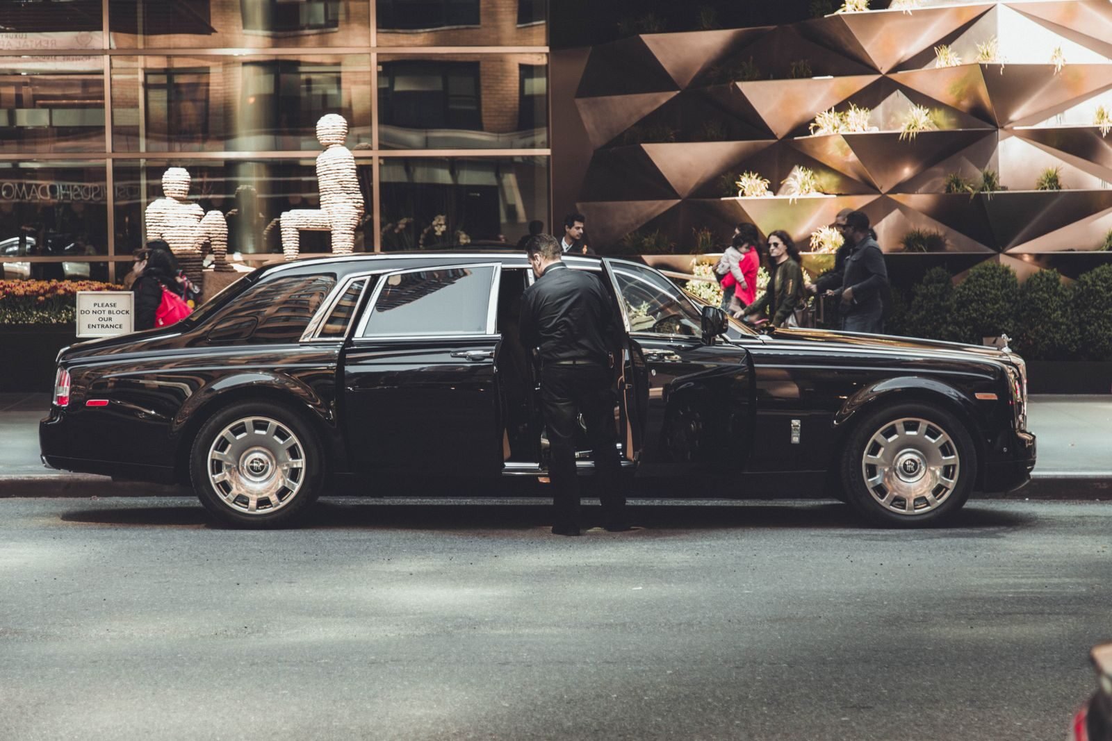 Elegant Rolls Royce with chauffeur outside modern building in New York City, illustrating luxury and class.